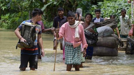 Orang-orang berjalan di air banjir di distrik Nagoon di negara bagian Assam, India pada 18 Mei.