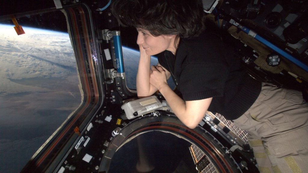 astronaut samantha cristoforett leaning on the multi-pane cupola window on the space station and looking outside