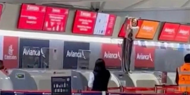 Penumpang lain di bandara dapat melihat orang yang lepas kendali - berdiri di konter check-in dan memegang layar di atasnya - dari jauh.